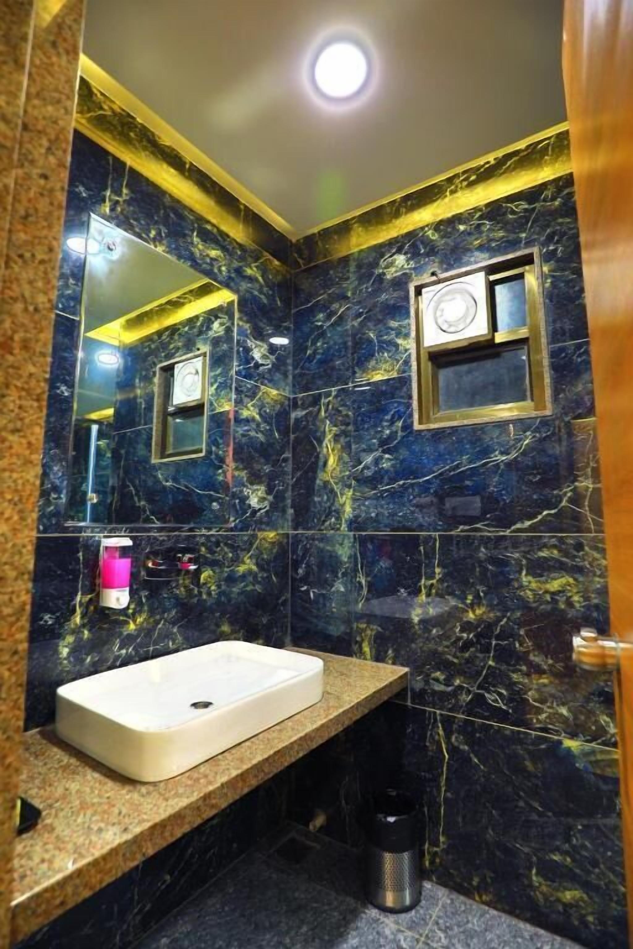 A bathroom with a marble wall, a sink, a mirror, and a small window.