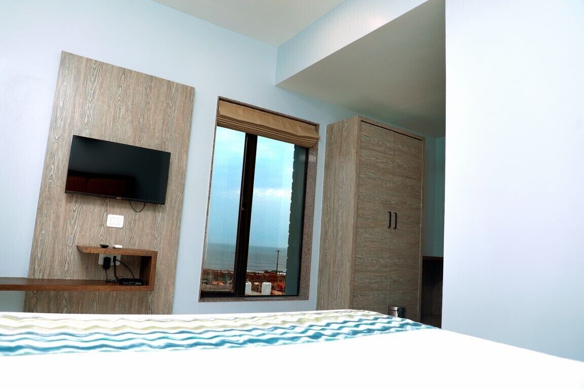A modern bedroom with a built-in TV, a large window with a view, and a wardrobe.