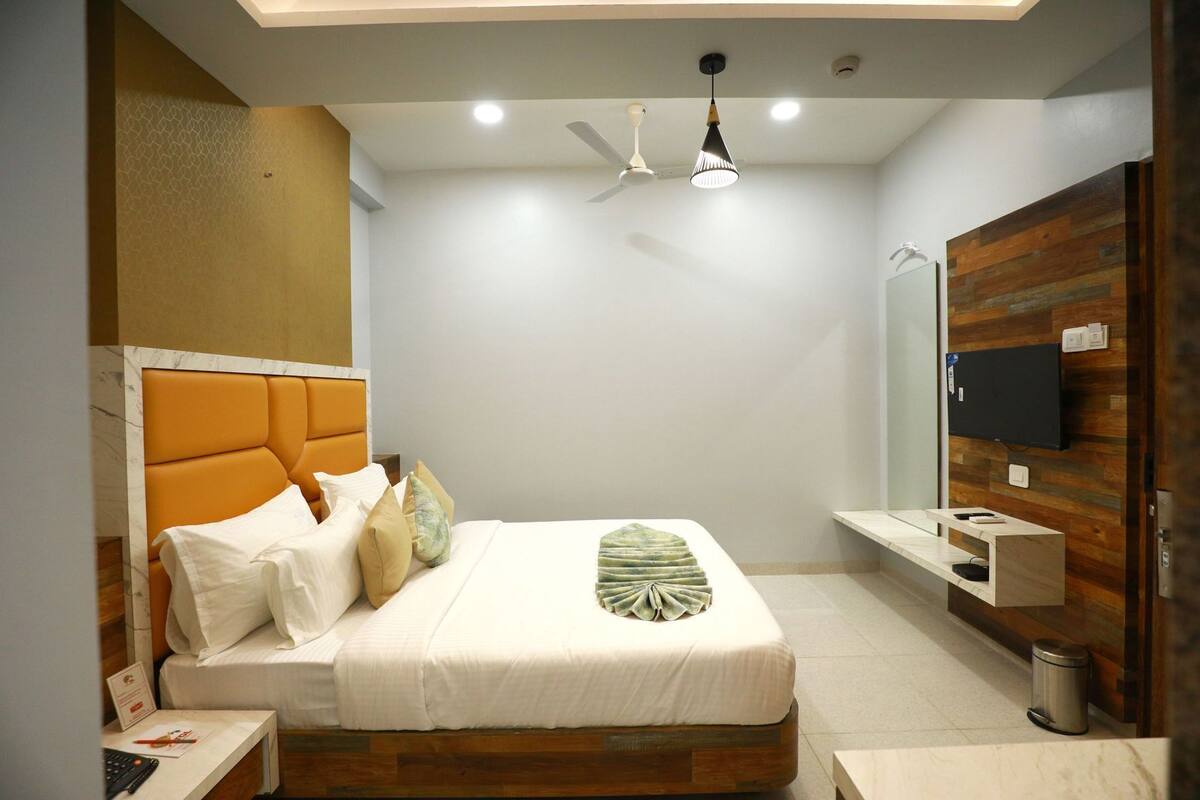 Quarto moderno com cama, mesas de cabeceira, ventilador de teto, televisão e parede de destaque em madeira.