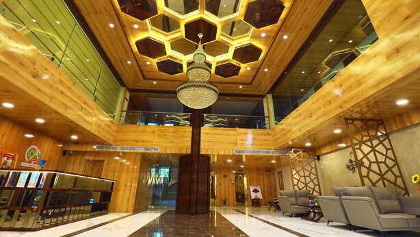 A lobby with a wooden interior, a central chandelier, and a reception desk. - Hotel The Grand Ladhukara (Dwarka)
