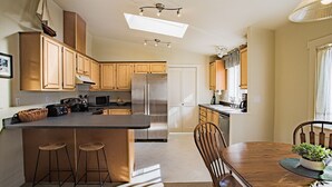 Eine moderne Küche mit Holzausstattung, einem Edelstahlkühlschrank, einer Essecke mit Holztisch und -stühlen sowie einer Pendelleuchte.