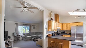Eine moderne Küche mit Holzschränken, einem Edelstahlkühlschrank, einer Mikrowelle und einer integrierten Kücheninsel mit Sitzgelegenheiten.