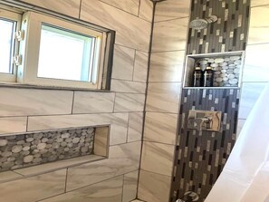 A bathroom with a window, a built-in shelf with toiletries, and a pebble wall.