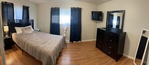 A bedroom with a bed, a dresser, a TV, and curtains.