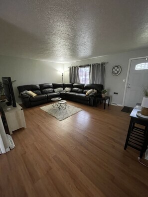 A living room with a black leather sofa, a coffee table, and a television on a stand.