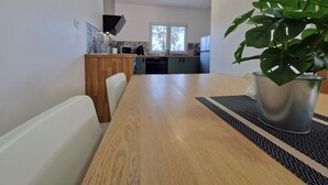 A modern kitchen with a wooden dining table, a potted plant, and a clock on the wall. - Gîte en Sologne - La Deniserie + Garage (Romorantin-Lanthenay)
