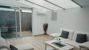 A modern living room with a white sofa, a coffee table, and a sliding glass door leading to an outdoor area. - Gîte en Sologne - La Deniserie + Garage (Romorantin-Lanthenay)