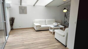 A modern living room with a white sofa, a small table, and a lamp. - Gîte en Sologne - La Deniserie + Garage (Romorantin-Lanthenay)