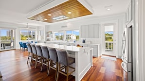 Una cocina amplia con una isla grande, muebles blancos y vistas al exterior.