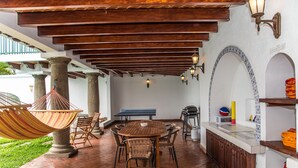 Un patio cubierto con una mesa y sillas de madera redondas, una hamaca y una parrilla.