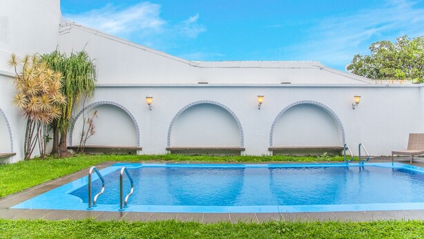 Una piscina con borde azul, rodeada por un edificio blanco con ventanas arqueadas y techo de tejas.