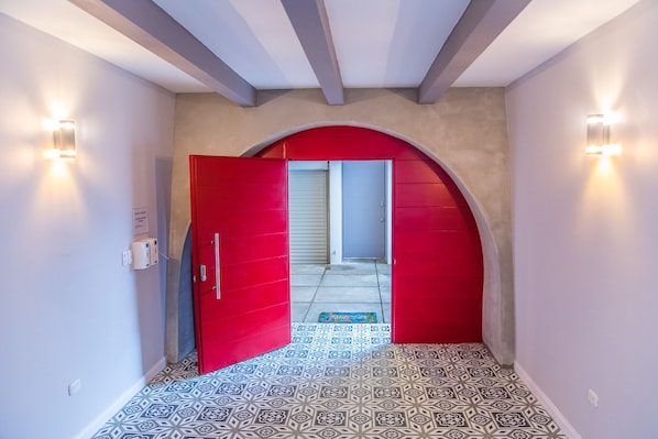 A hallway with patterned floor tiles, a red door, and a small rug.
