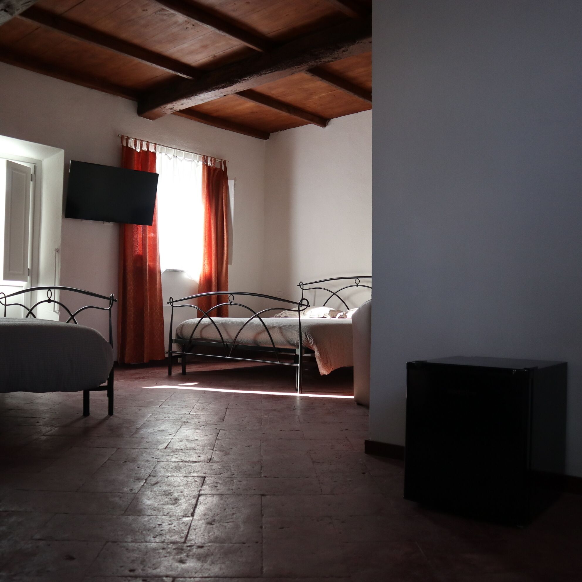 Ein Zimmer mit einem Bett, einem an der Wand montierten Fernseher und einem Vorhangfenster.