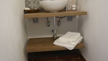 A bathroom with a white vessel sink, a wooden shelf, and a towel stack.
