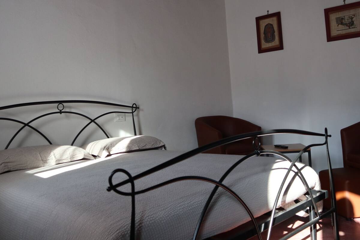 A bedroom with a metal bed frame, a wooden ceiling, and two framed pictures on the wall.