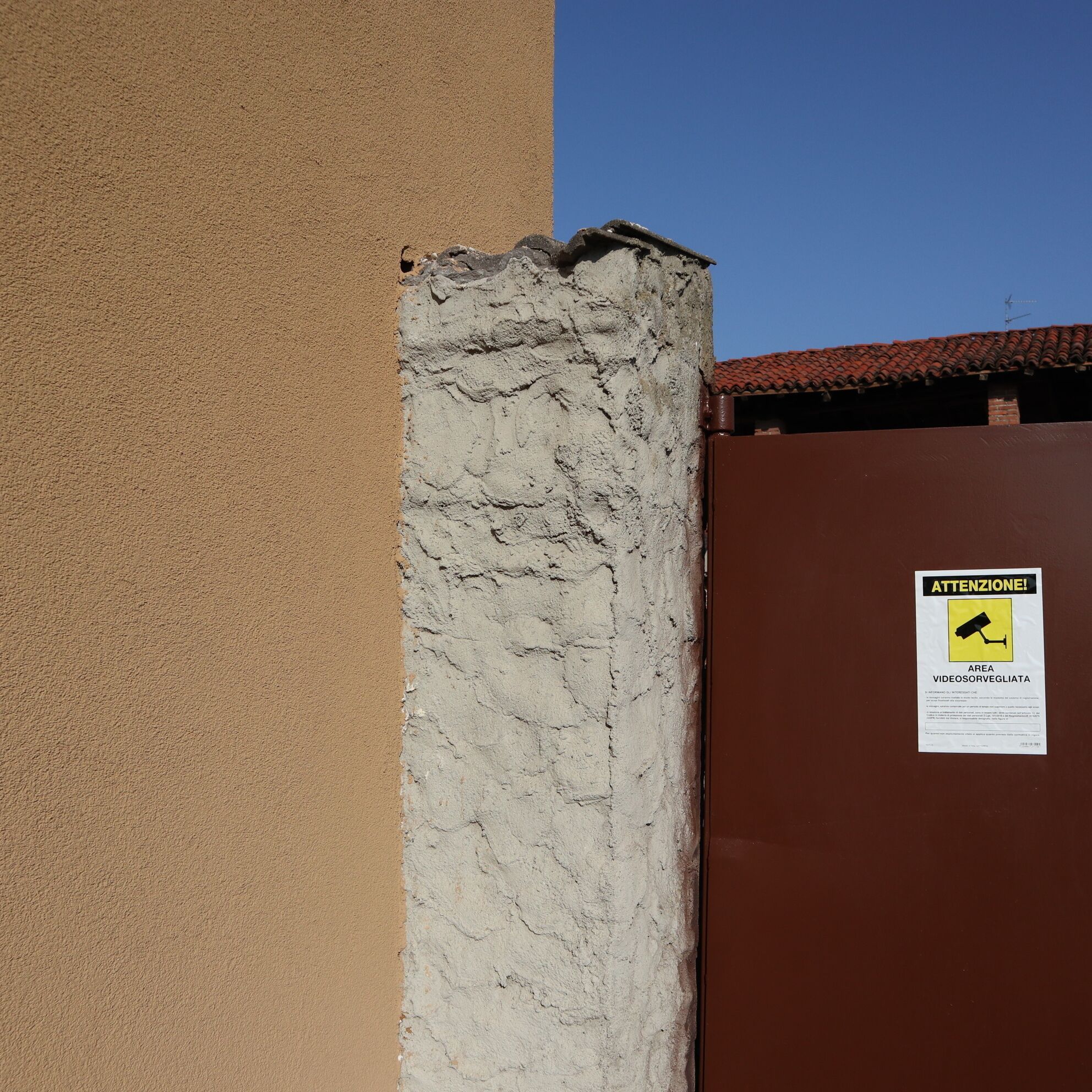 Um portão metálico marrom com uma placa de aviso sobre vigilância.