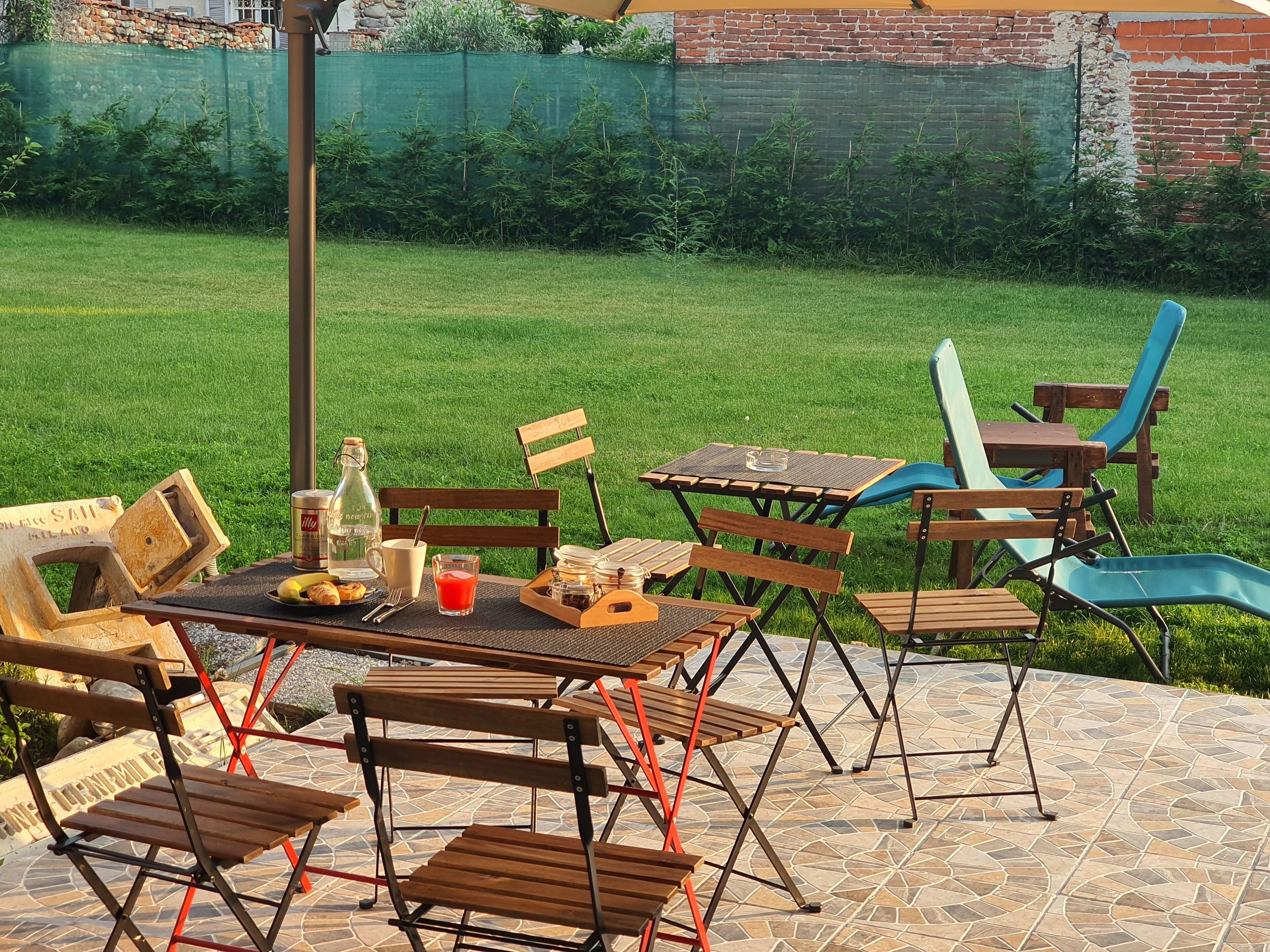 Un patio al aire libre con una mesa dispuesta para dos personas, rodeado de sillas de madera y un sillón azul.