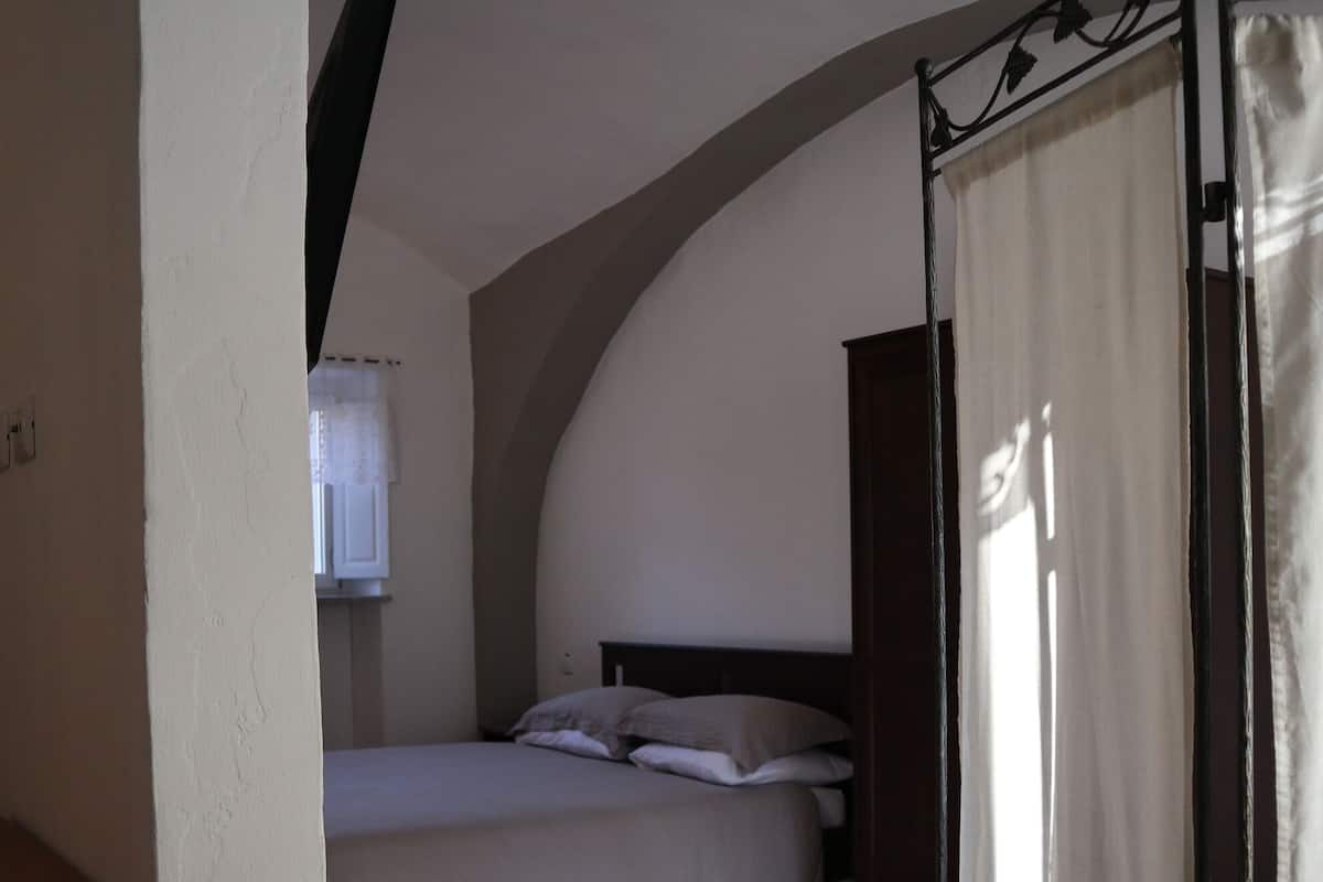 A bedroom with a bed, a window with a curtain, and a tiled floor.