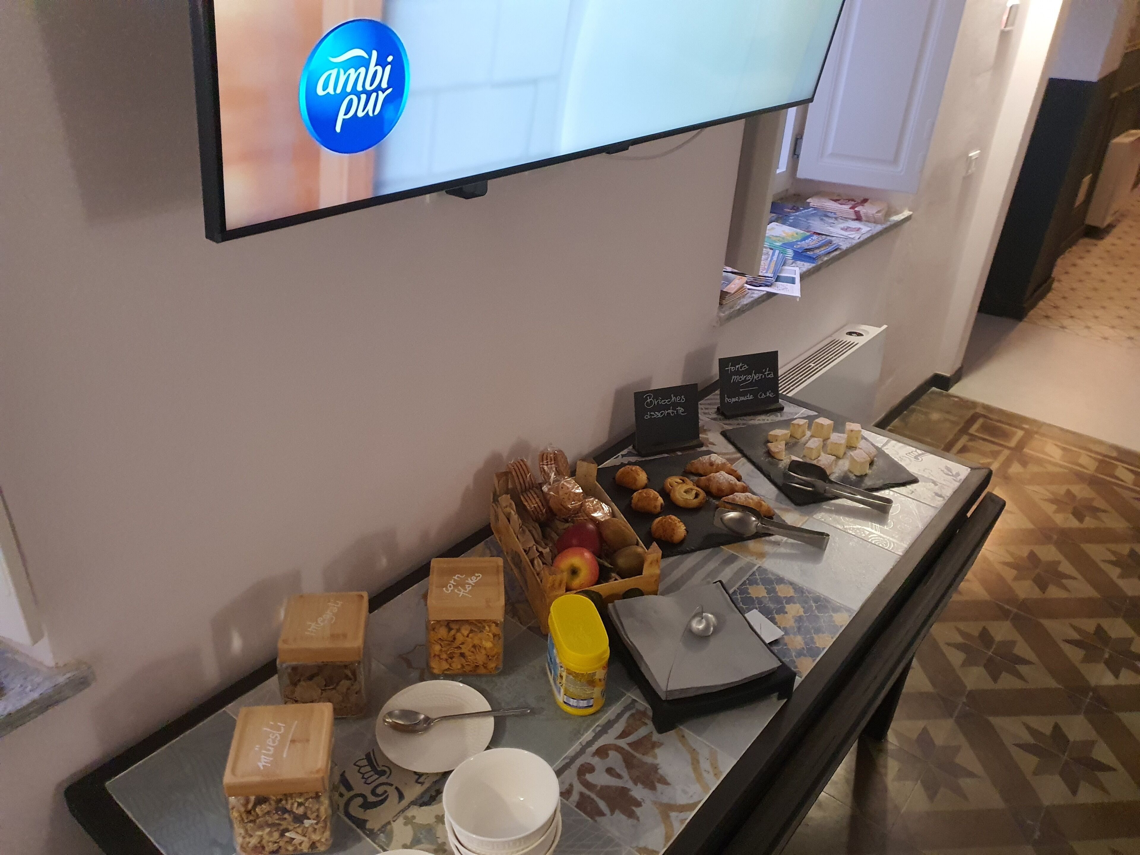 Un bufé de desayuno con diversos alimentos y un televisor mostrando 'ambi pur'.