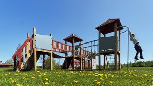 A playground with a climbing structure and slides, set in a grassy field with yellow flowers. - Juku Dzirnavas (Saldus district)