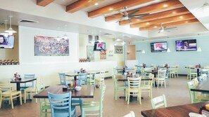 Un restaurante espacioso con varias mesas y sillas, ventiladores de techo y televisiones fijadas a la pared.