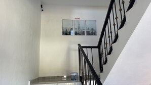 Una escalera con barandillas negras y una pared blanca. Hay tres cuadros en la pared, uno de los cuales muestra un cartel de 'No Smoking'.