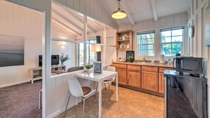 Una cocina moderna con armarios de madera, un comedor con mesa y sillas blancas, y un ventanal que proporciona luz natural.