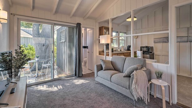 Una sala de estar moderna con un sofá gris, una mesita y un ventanal de vidrio que da a un patio.