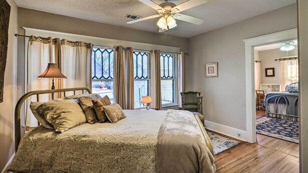 A bedroom with a bed, a ceiling fan, a window with curtains, a chair, and a door leading to another room. - Georgetown Vacation Rental Close to Town Square! (Georgetown)