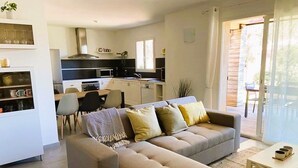 A modern living room with a sofa, a dining table, and a kitchen in the background. - Appartement Lena. 6 pers,  piscine, 500 m plage (SAINTE LUCIE DE PORTO VECCHIO)