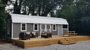 Une petite cabane dotée d’une terrasse, aménagée avec des chaises en osier et une table de pique-nique.