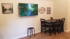 Un coin repas comprenant une table et des chaises, un petit tabouret, un téléviseur fixé au mur et un élément décoratif en bois.