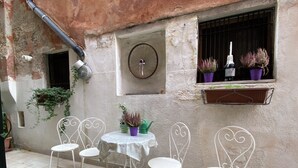 Ein Innenhof mit einem runden Tisch, vier Stühlen, einer Wanduhr und Blumentöpfen auf einem Fensterbrett.