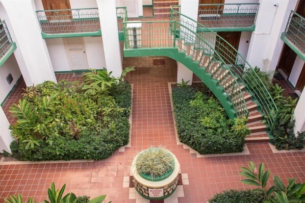 A multi-level atrium with a central staircase, surrounded by lush greenery and a tiled floor.