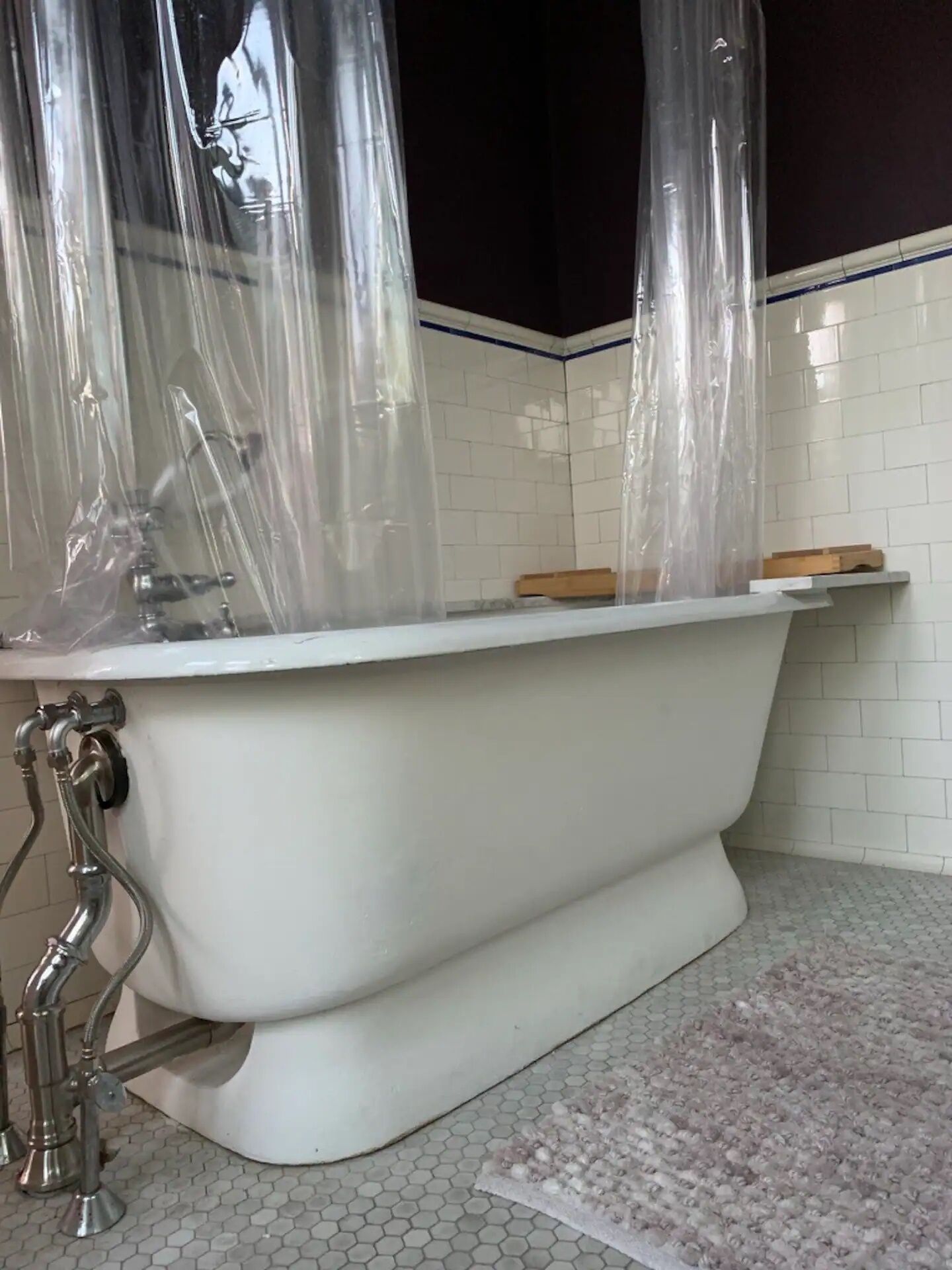 A white freestanding bathtub with chrome fixtures, a wooden soap dish, and a tiled floor with hexagonal patterns.