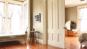 A room with a wooden floor, a chair, a table with a lamp, a framed picture on the wall, and a dresser with a mirror. - The Wedding Cake House (Providence)