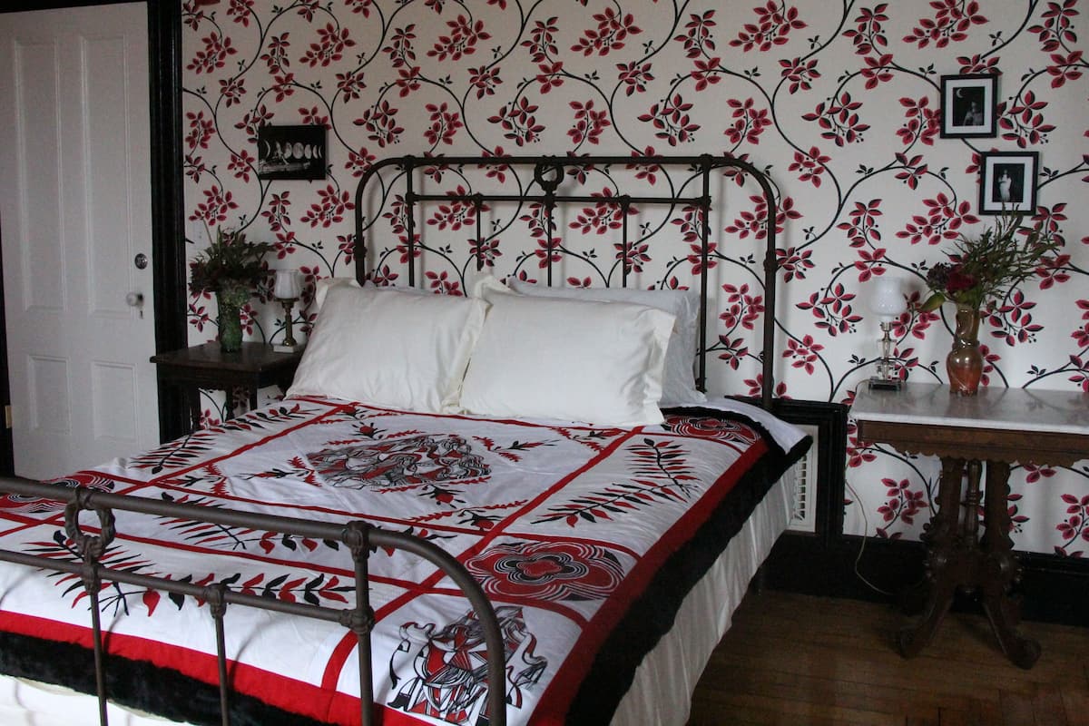 A bedroom with a bed, a nightstand, a dresser, and a floral wallpaper pattern.
