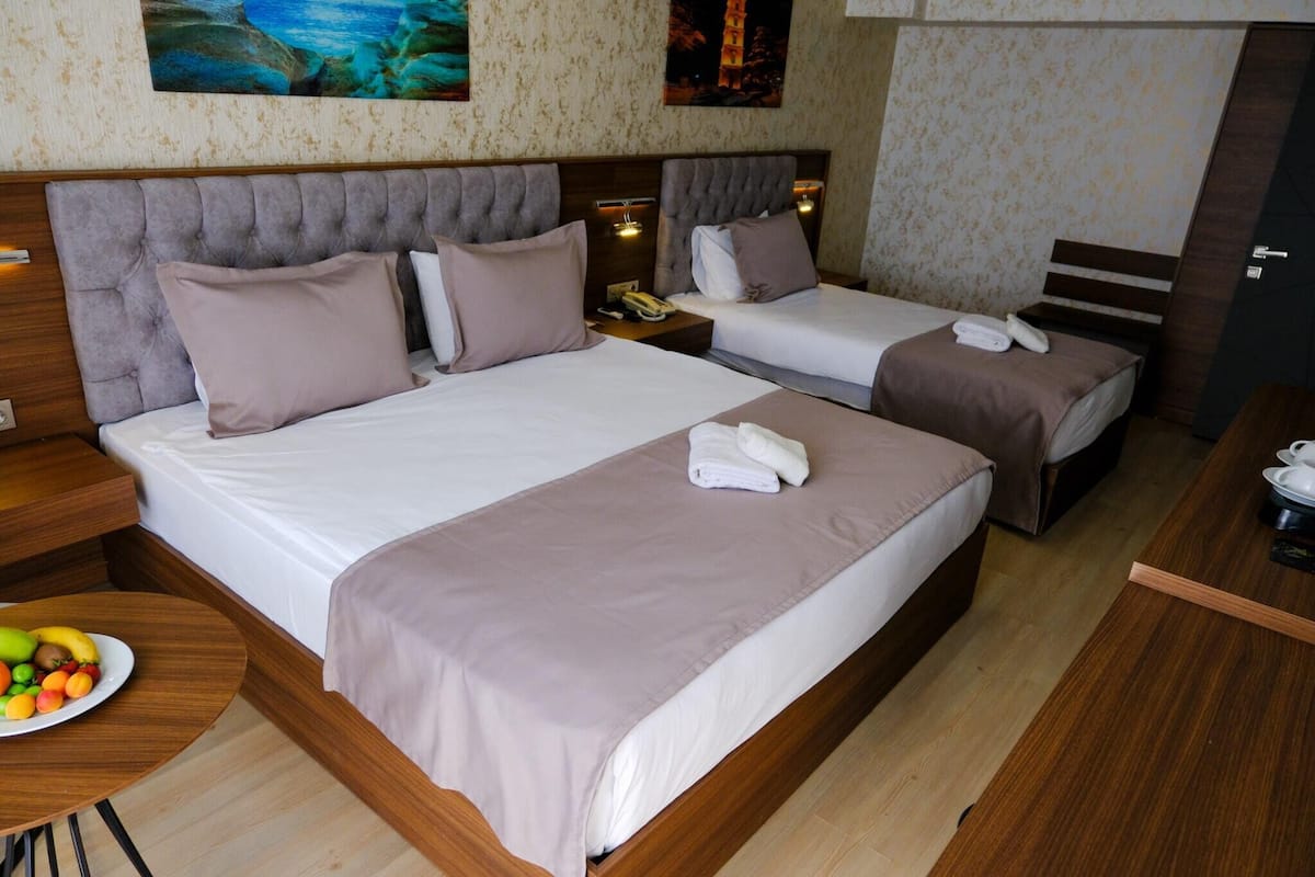 A hotel room with two beds, a wooden headboard, a bedside table with a fruit bowl, and a small desk with a telephone.