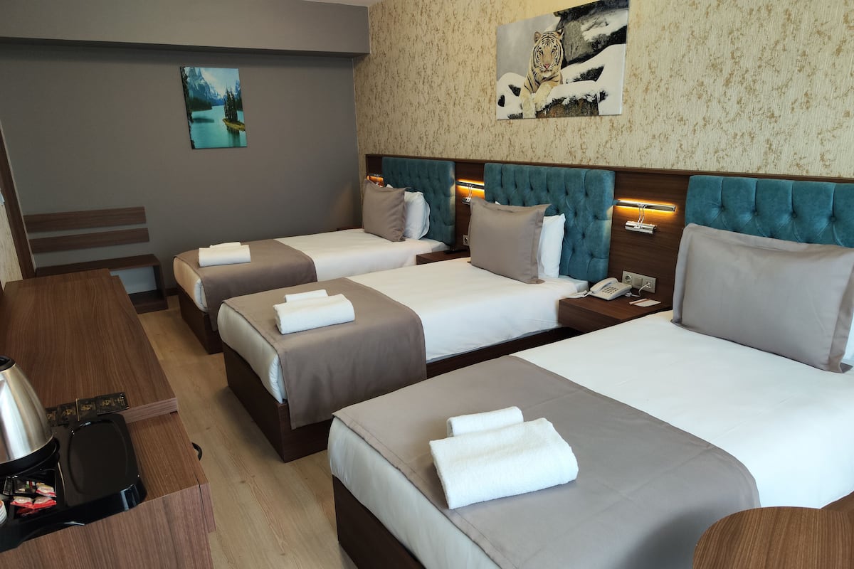 A hotel room with three beds, a wooden desk, and a coffee machine.