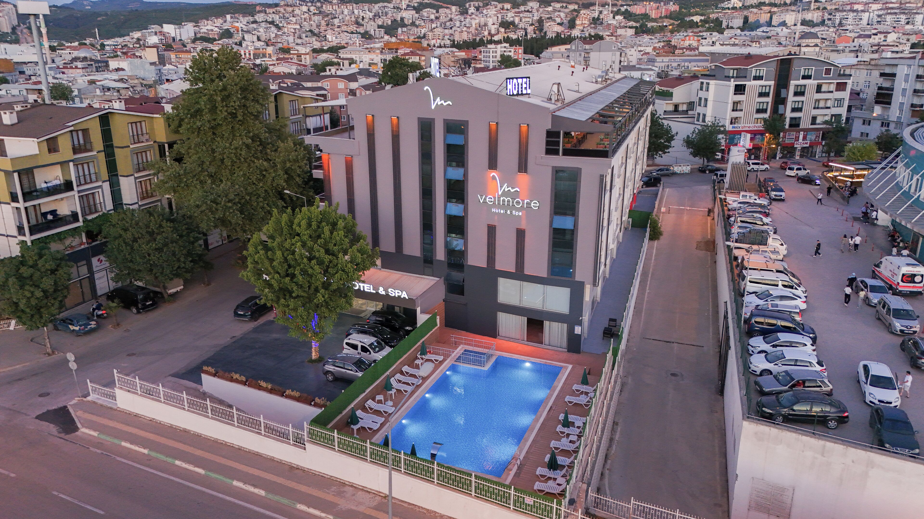 A hotel with a rooftop pool, surrounded by parked cars and a cityscape in the background.