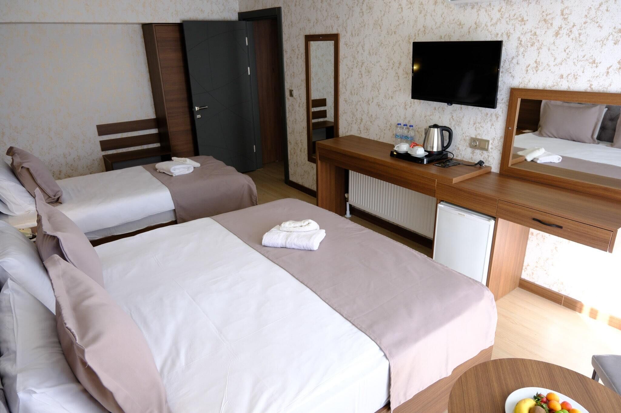 Una habitación de hotel con dos camas, un escritorio con espejo, televisor y un refrigerador pequeño.