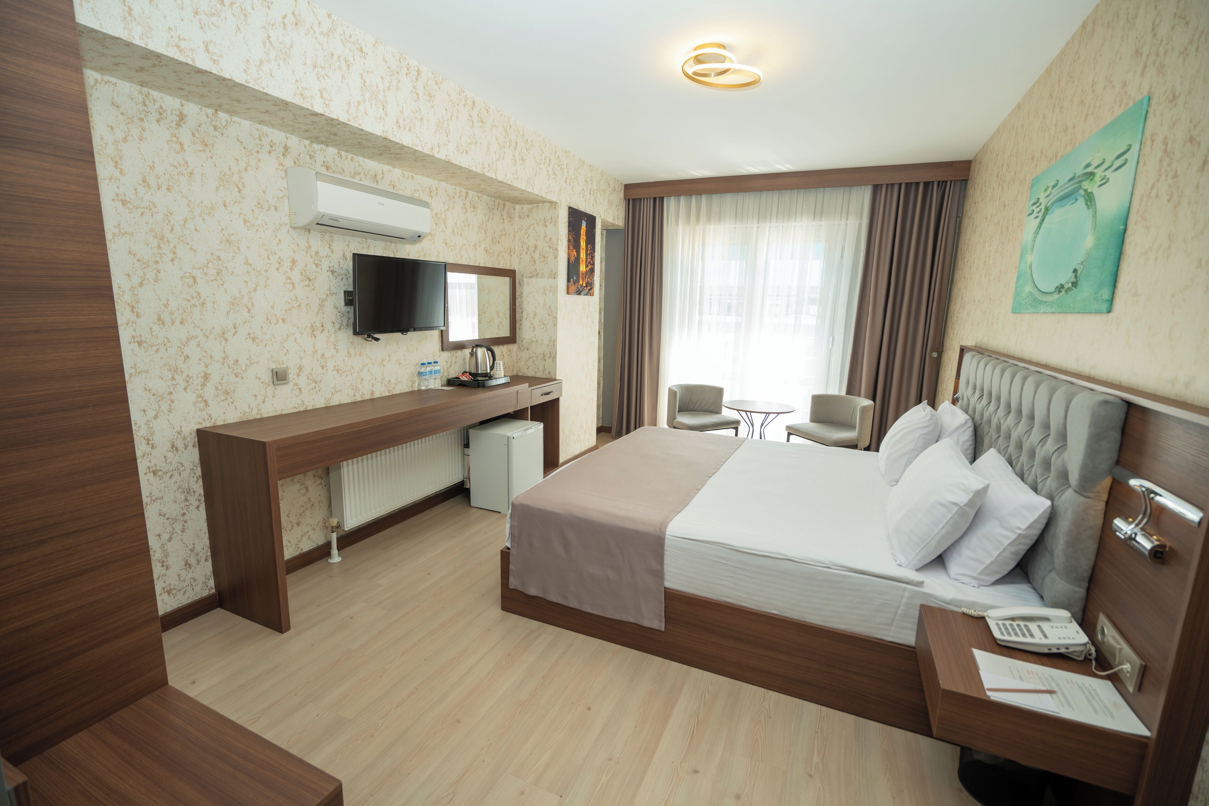 Habitación de hotel con cama, escritorio, silla, televisor y ventana con cortinas.