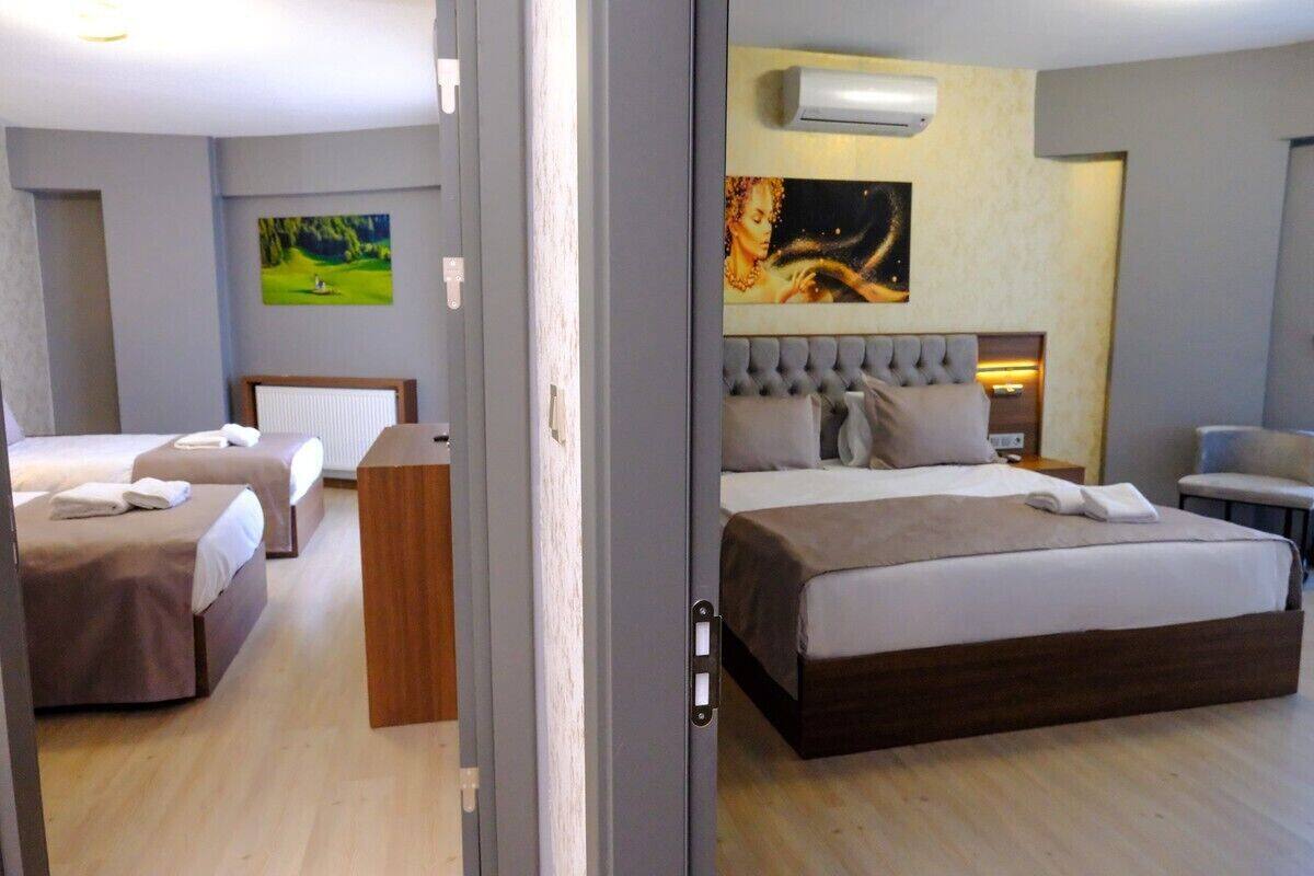 A hotel room with a large bed, two smaller beds, a wooden desk, and artwork on the walls.