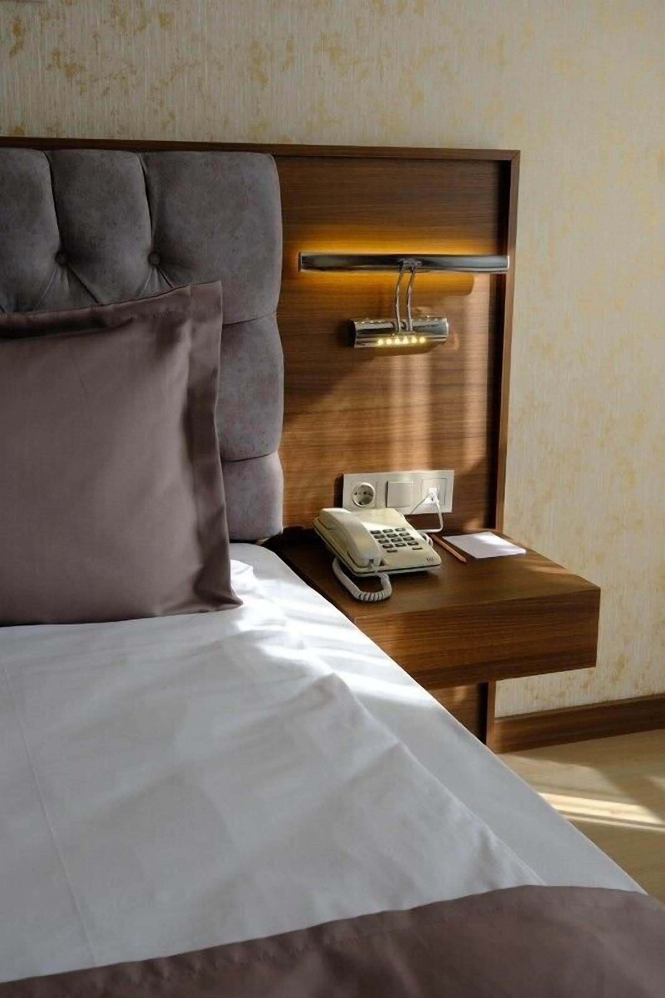 A hotel room with a tufted headboard, a bedside table with a telephone, and a lamp.