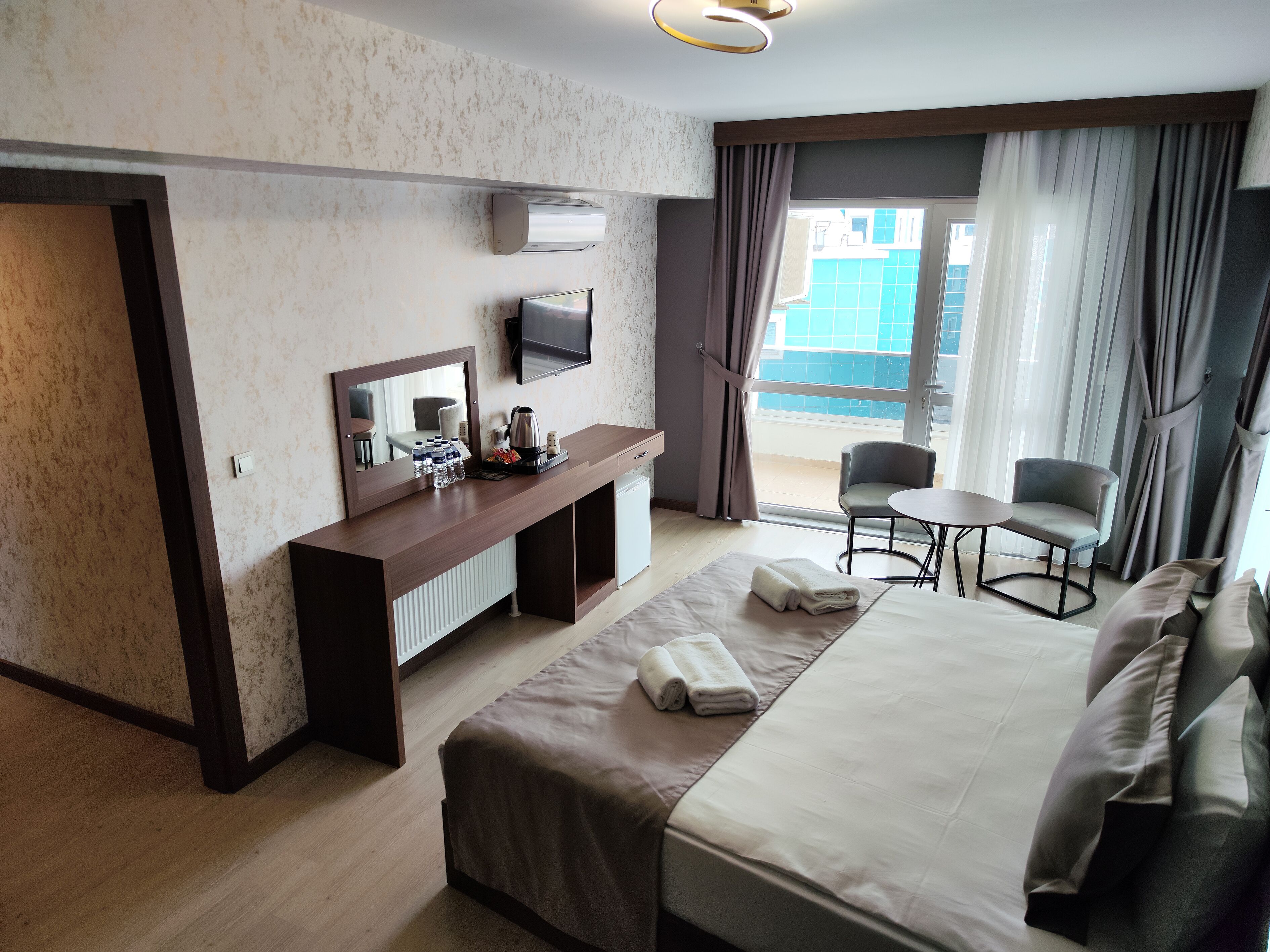 Habitación de hotel con cama, escritorio con espejo, televisión y vista al exterior.