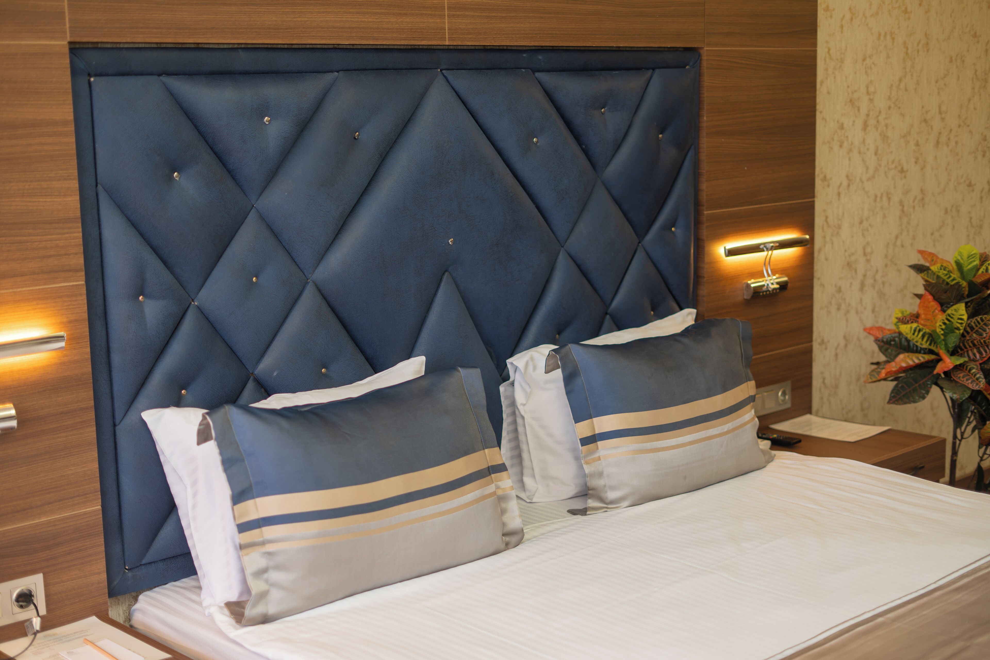 Una cama bien hecha con un cabecero capitonado, dos almohadas y una mesita de noche con lámpara.