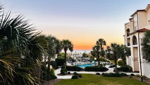 A resort with a pool, palm trees, and a view of the ocean at sunset. - Beachfront Capriani Resort, Private Balcony, Ocean Pool Views, Linens Towels (North Topsail Beach)