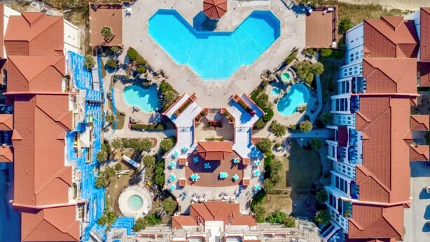An aerial view of a resort with multiple swimming pools, a central courtyard, and surrounding buildings with red-tiled roofs. - Beachfront Capriani Resort, Private Balcony, Ocean Pool Views, Linens Towels (North Topsail Beach)