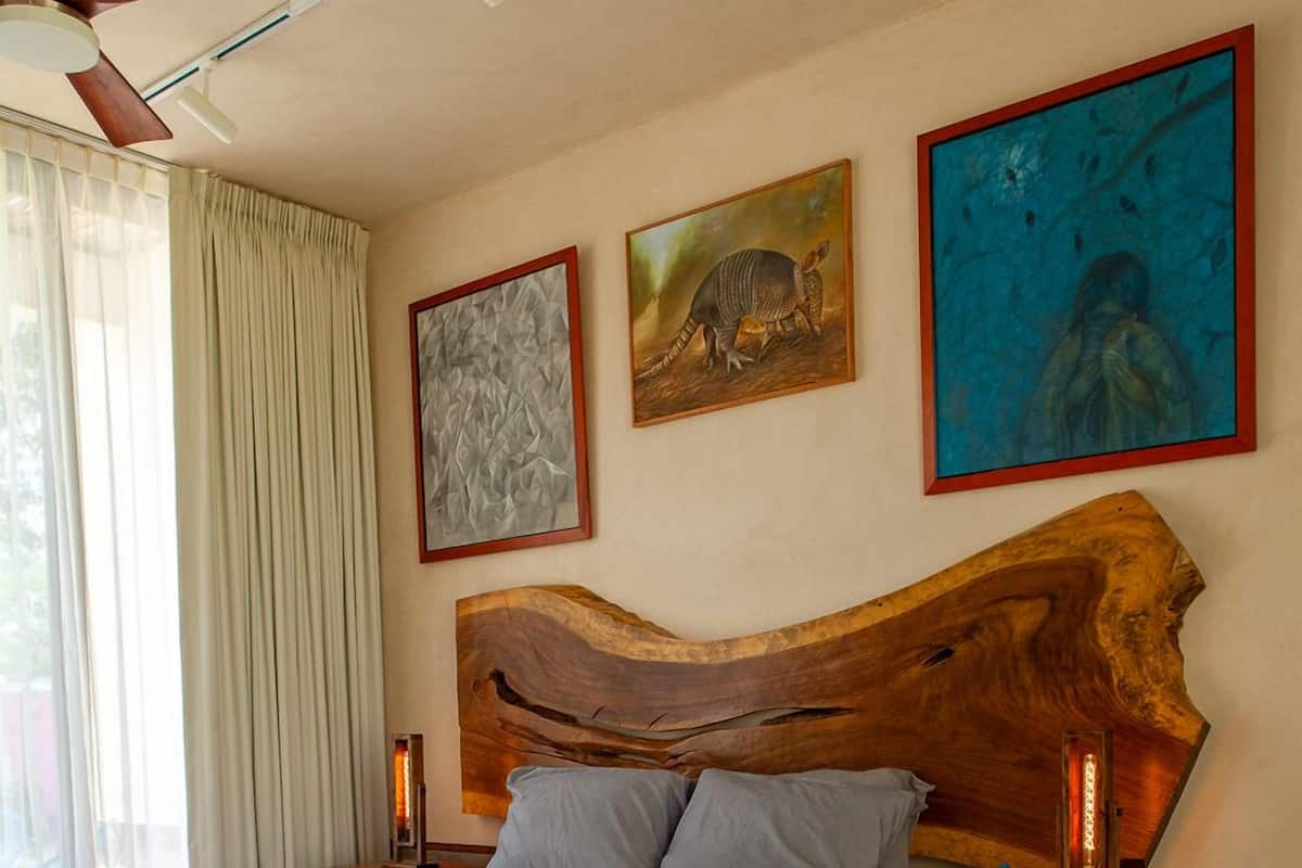 A bedroom with a large bed, wooden headboard, a round wooden table, and artwork on the walls.