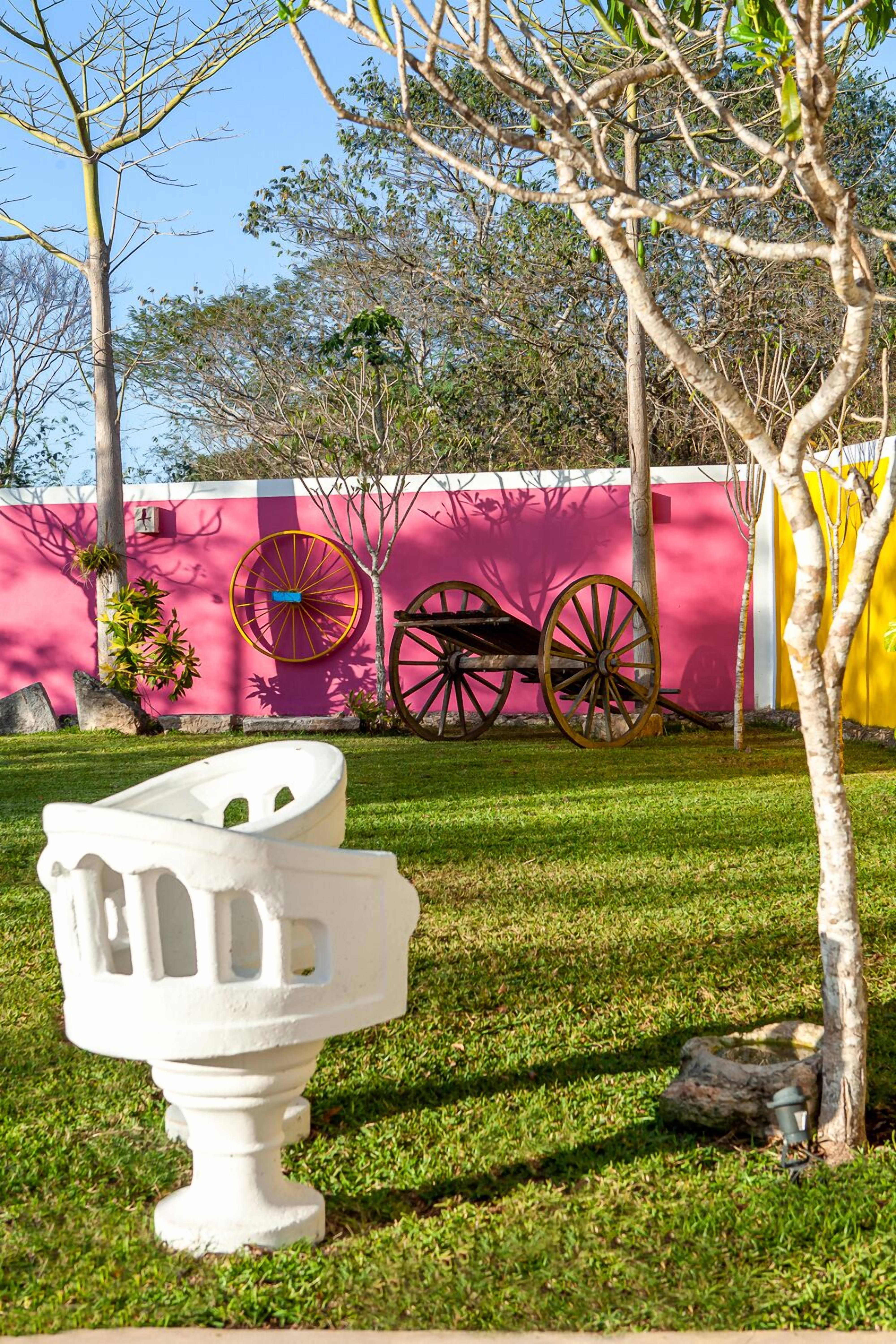 A white outdoor sculpture, a pink wall, and a tree in a grassy area.